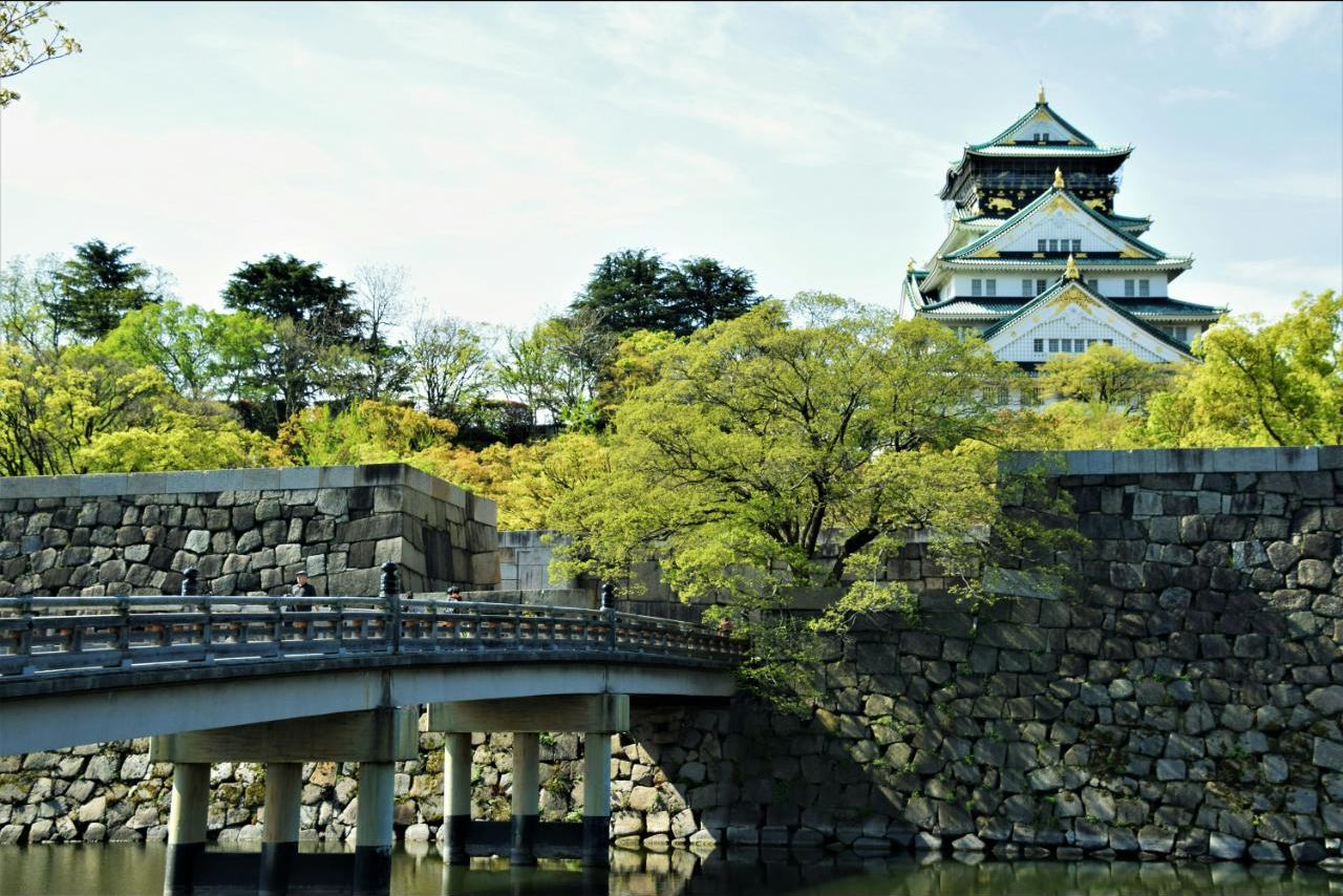 Osaka Castle's main tower rising above its stone walls and moat bridge, framed by spring greenery